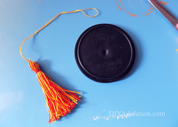 Lid with a hole in the center next to red and yellow tassel