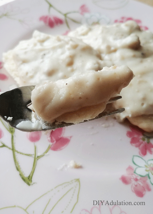 Forkful of biscuits and sausage gravy with plate of food in the background