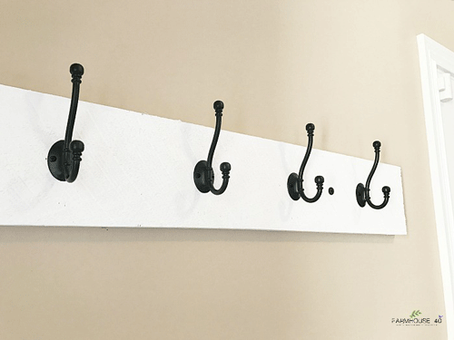 White wooden board mounted on a wall with black coat hooks on it