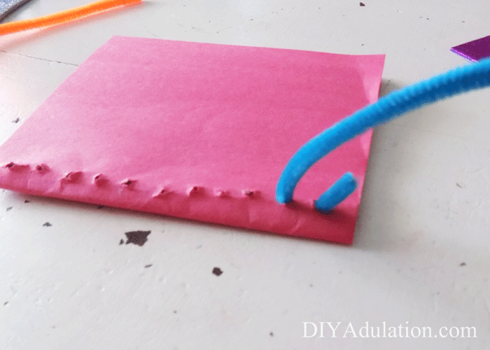 Threading chenille stem through holes in construction paper