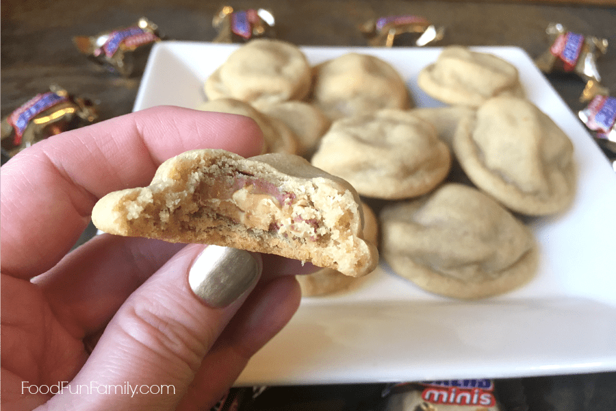 Hand holding Snickers Stuffed Peanut Butter Cookie with Bite Out of It