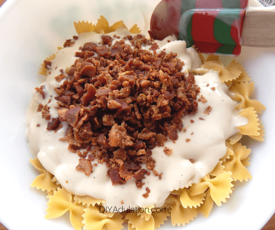 Bacon and Alfredo Sauce in Bowl of Uncooked Bow Tie Pasta