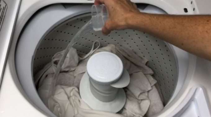 Hand pouring liquid into open washer drum